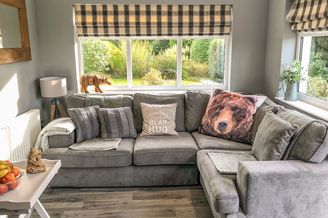 Snug at Penlaurel with bear cushions, grey sofa and views of the garden.