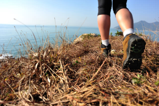 Person wearing walking boots walking along coast with sea in background