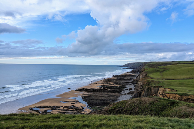 The long beach at Sandymouth Bay, with dark rocks at the top and golden sand closer to the sea.