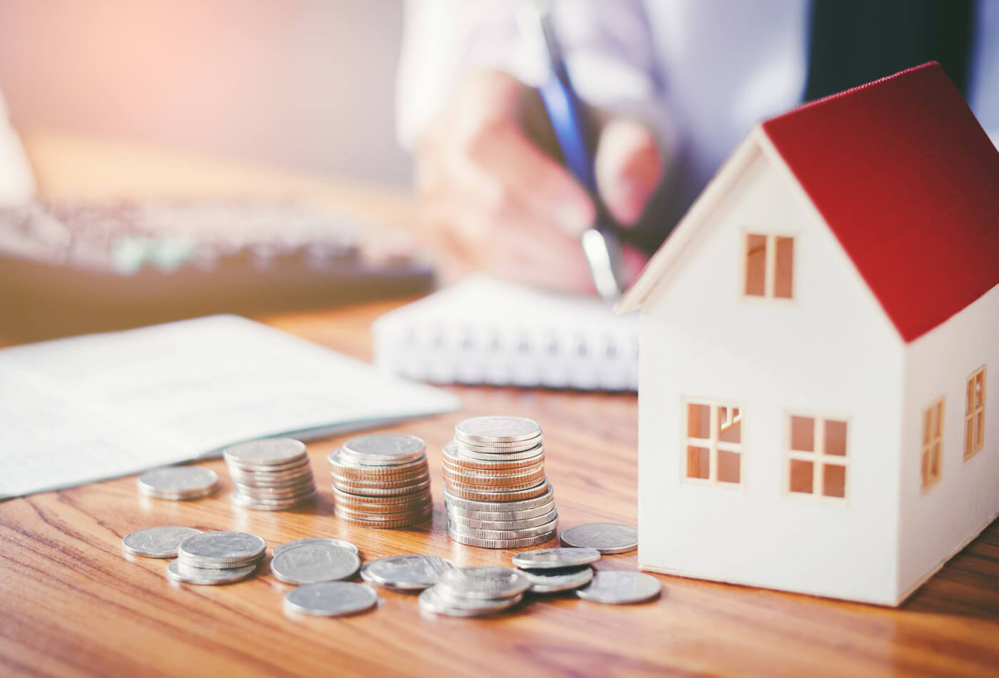 model house on desk with money and a man working out finances.