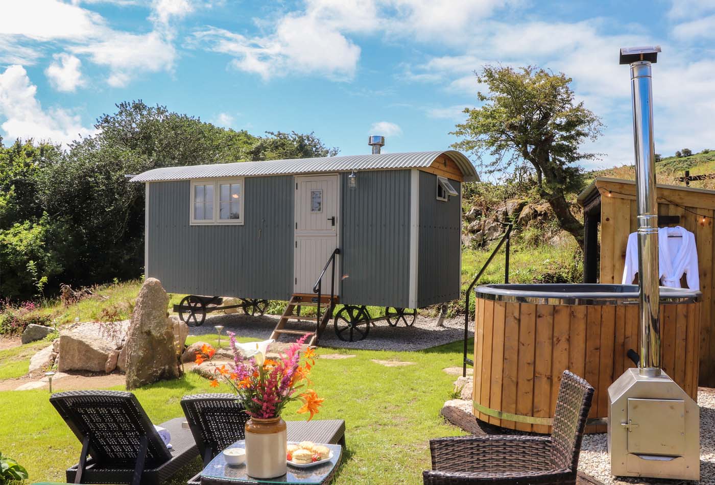 Outside view of Bosulla Shepherds Hut, Penzance, with a hot tub and deck chairs in front.