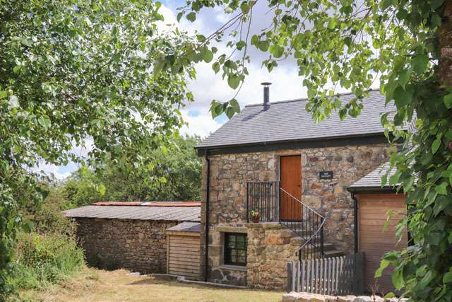 Stone barn conversion with steps to the entrance and leafy branches in the foreground
