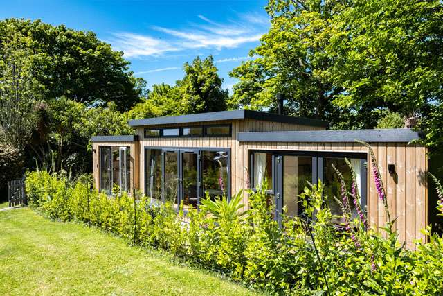 Modern wood-clad holiday lodge with glass frontage, surrounded by bright green foliage