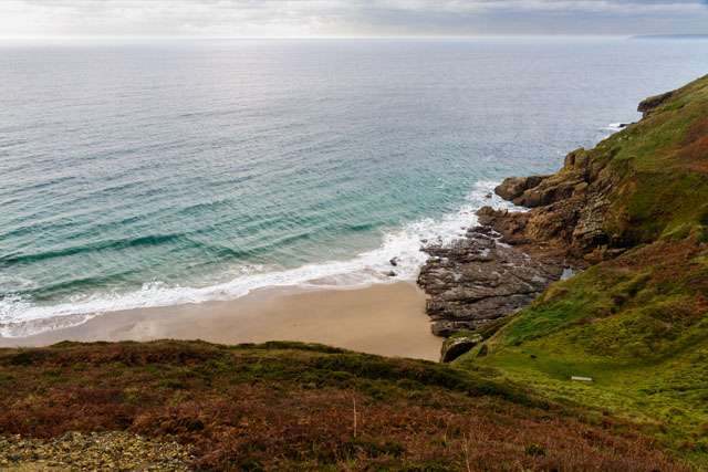View down over steep grassy slope, with golden beach and sea at the bottom