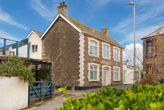 Outside view of a large detached house on a sunny day, with foliage in the foreground
