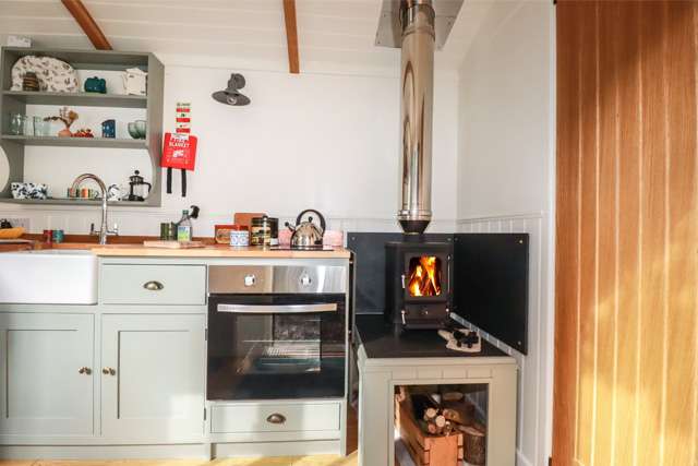 Pale blue kitchen with a small wood burner in a Shepherd's hut